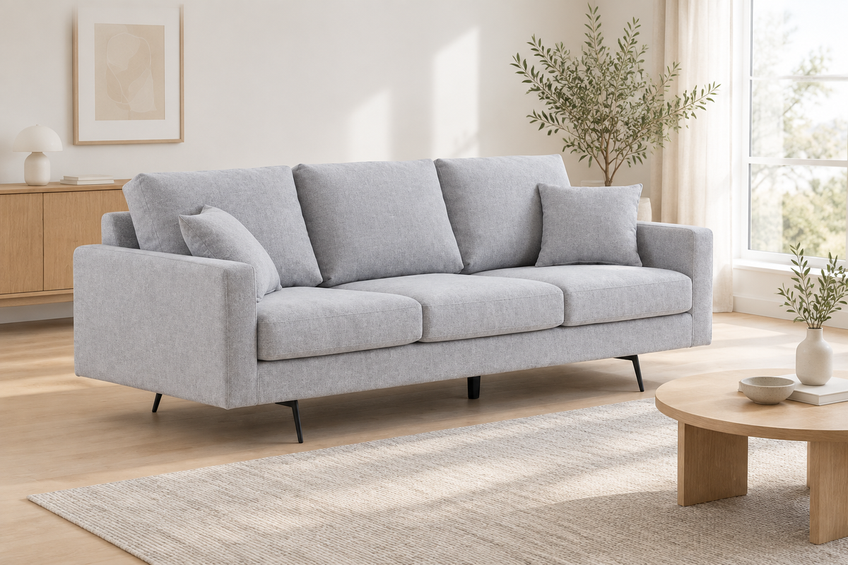 Canapé trois places gris clair avec deux coussins, photographié de trois quarts dans un salon scandinave lumineux.