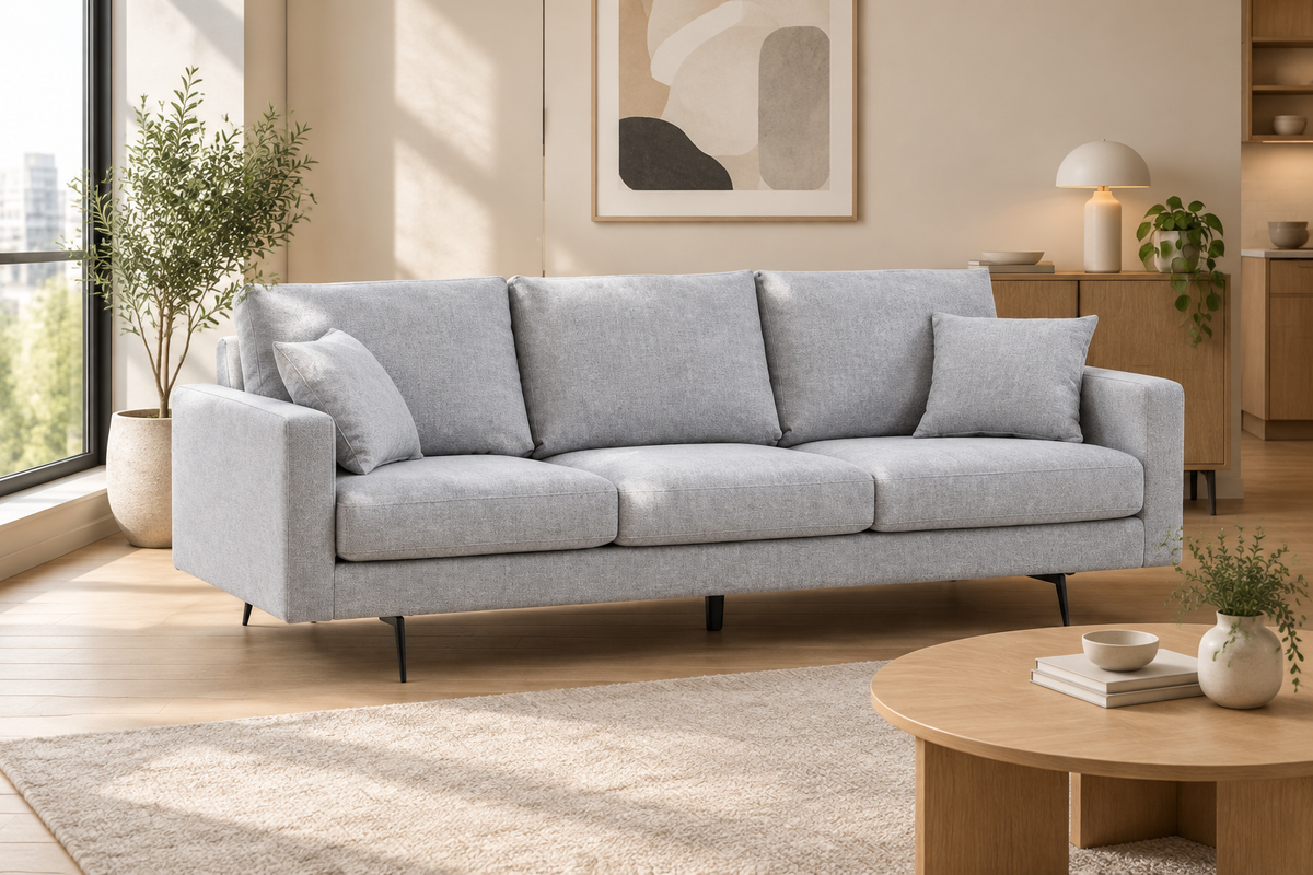 Canapé trois places en tissu gris clair avec deux coussins, dans un petit salon lumineux.